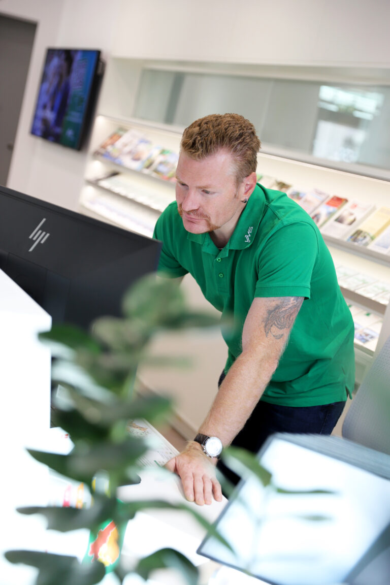 Ein Kundebetreuer des VMS im grünen Shirt bedient im Kundencenter einen PC
