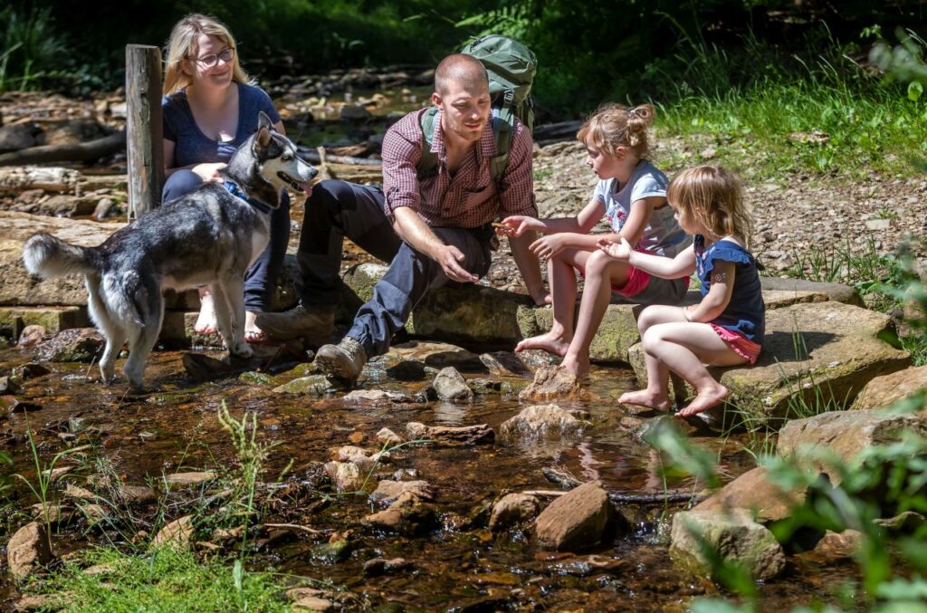Eine vierköpfige Familie mit Hund sitzt am Fluss