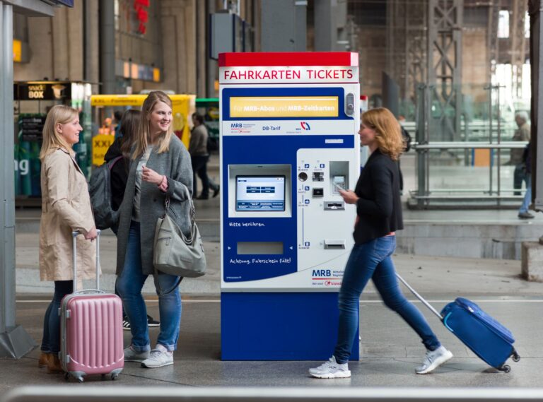 Mehrere lächelnde Personen stehen neben einem Fahrkartenautomaten der MRB