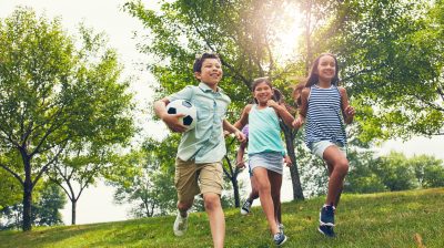 Kinder rennen mit Ball im Arm im Grünen