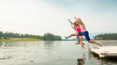 Kinder springen mit ausgestreckten Armen in einen Badesee