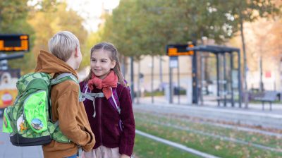 Auf dem Weg zur Schule: Zwei Grundschulkinder mit Ranzen warten an der Haltestelle
