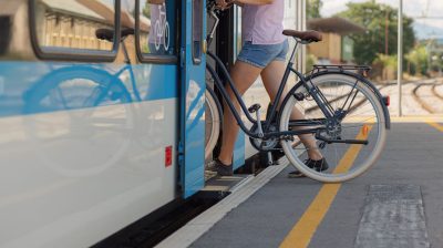 A cyclist prepares to board a train with a bicycle at a busy station during daytime, showcasing sustainable transport.