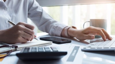 Business women using computer and calculator during note some data on notepad for calculate financial at home office